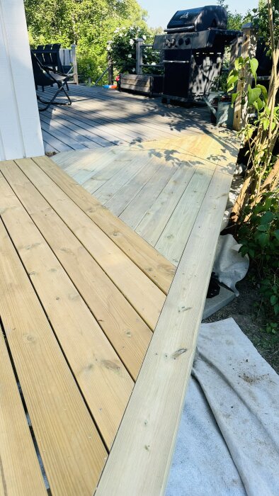 Tralldäck i anslutning till hus med ny och gammal trall integrerad, grill och utemöbler i bakgrunden.