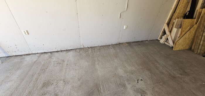 Garaget med en betongplatta som visar en stor spricka längs väggen, med trämaterial staplat i hörnet.