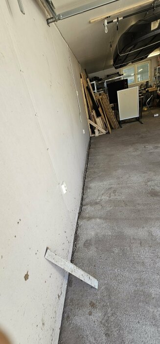 Bild på en betongplatta i ett garage med en synlig spricka längs väggen och en vinkelhake som visar sprickans position.
