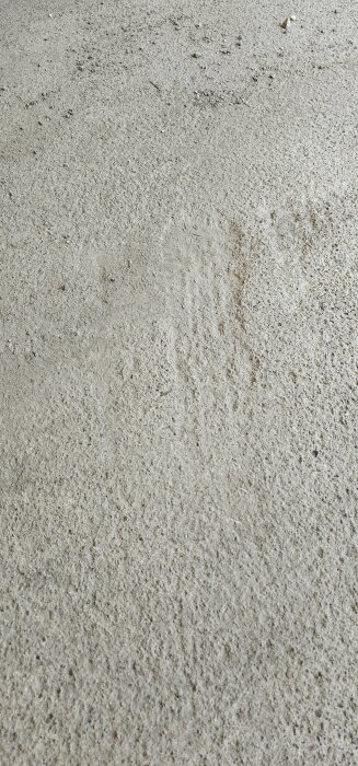 Närbild på en sprucken och ojämn betongplatta med synliga småstenar och skrovlig yta.