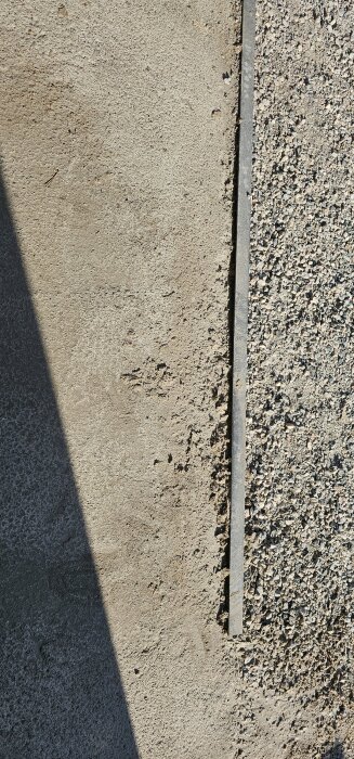 Stor spricka i betongplatta för garage, nära väggen, med ojämn yta och små gruspartiklar.