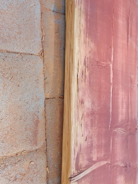 En träregel med fuktangrepp mot en rosa vägg och en tegelvägg.