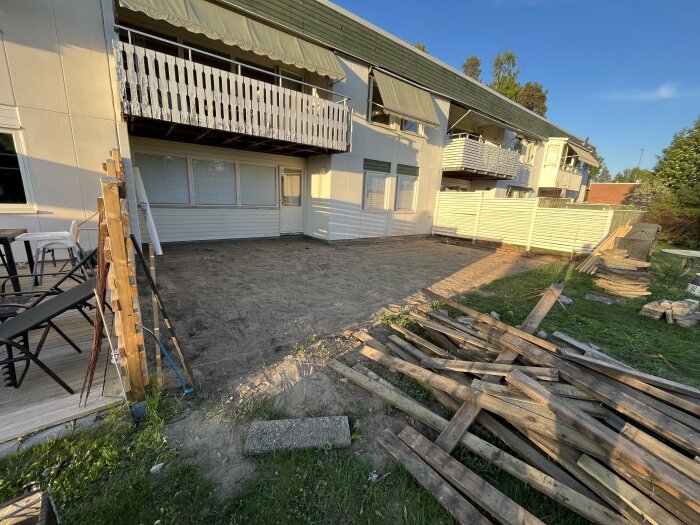 Jord uppkörd bredvid hus med trallveranda och trädgårdsmaterial ssom ligger utspridda.