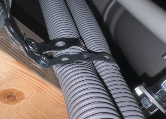 Rör-i-rör-system med metalldetaljer fastsatta på träyta och synliga förskruvningar.
