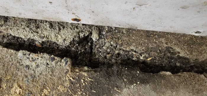 En sned spricka i en betongkonstruktion med synlig jord och berggrund nedanför.