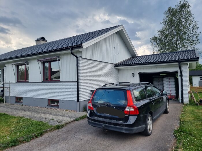 Ett hus med nyligen målad panel i kulören 0502-Y, grå grundmur och svart tak, med en bil framför på uppfarten.