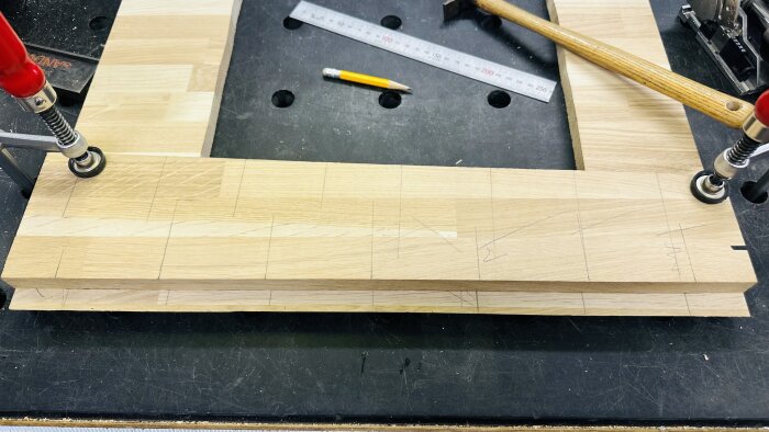 Träplanka fastspänd på arbetsbänk med utritade markeringar, tillsammans med verktyg.