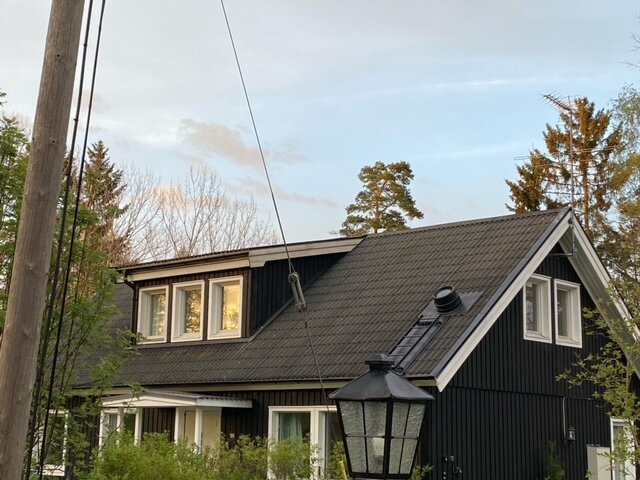 Ett svart tak på ett tvåvånings hus med lutande taklinje och fönster mot en skymningshimmel.