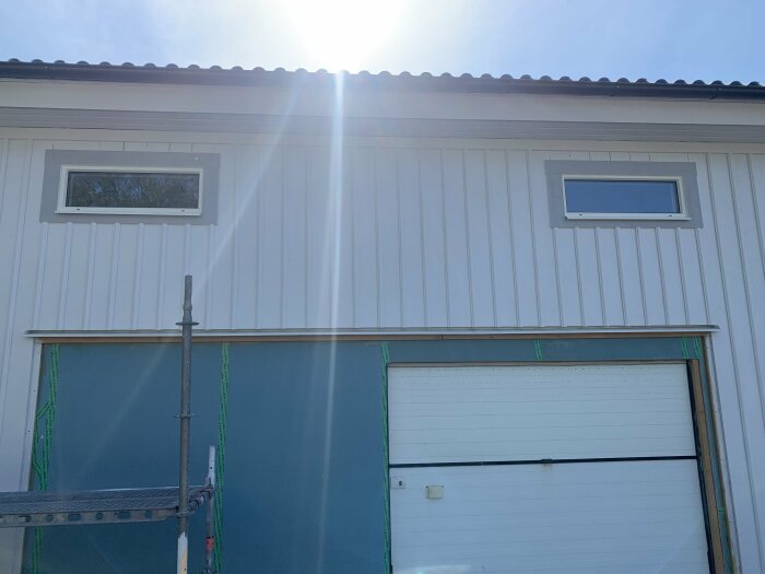 Nyinstallerade plåtar och foder kring tre fönster på en vit garagebyggnad i solljus.