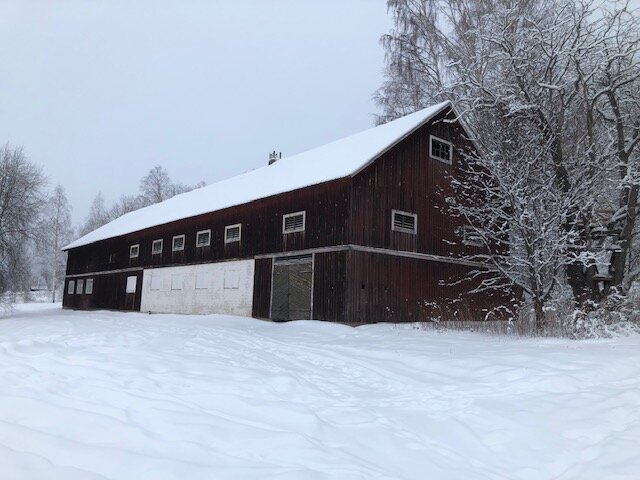 Gammal stor lada i två plan omgiven av snö, träfasad, vitt landskap, inga synliga spår av kontaminering.