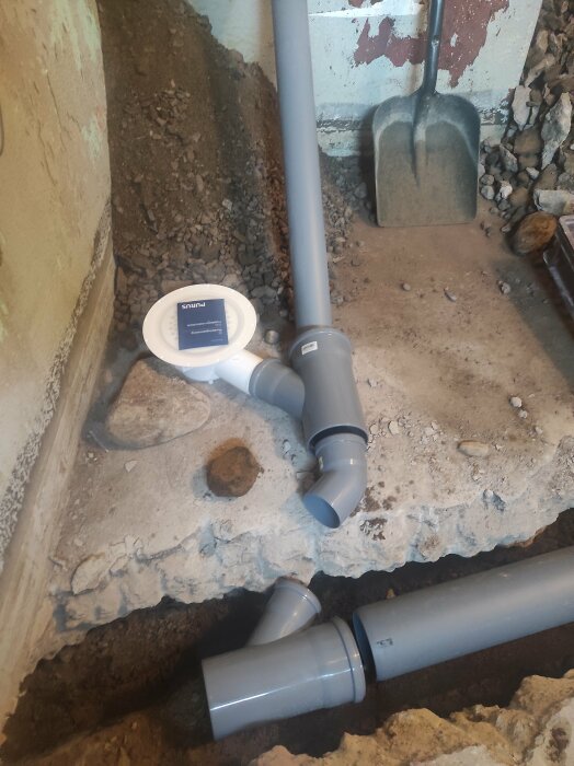 Renovering av tvättstugans avloppssystem i källare med nya gråa PVC-rör och Y-kopplingar synliga bredvid en schaktad betonggolv.