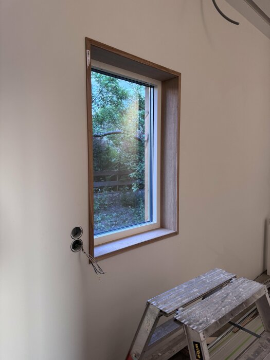 Oslipt och obehandlat fönster med ekfoder och synlig planhyvlad eklist vid en byggarbetsplats.