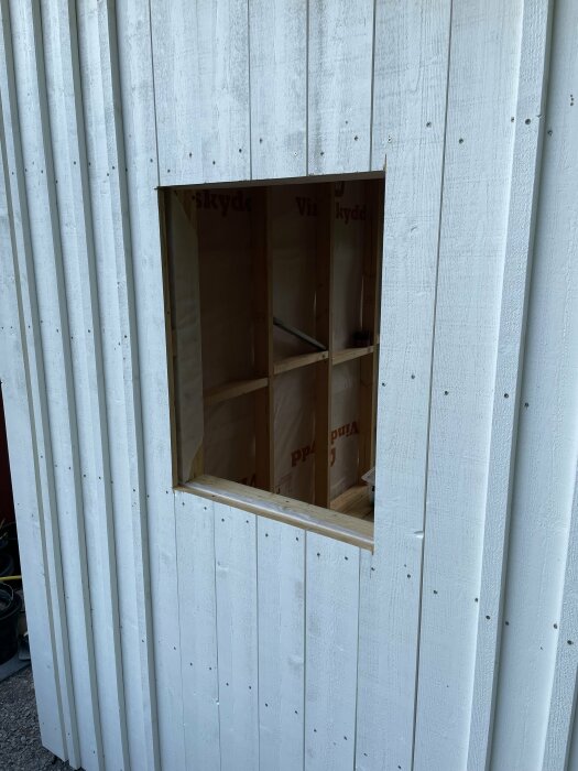 Förråd under konstruktion med öppet fönsterutrymme i en vit profilerad plåtvägg.