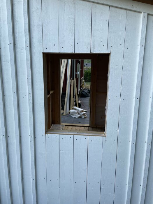 Öppet fönsterutrymme utan glas i en vit trävägg på ett förråd under konstruktion.