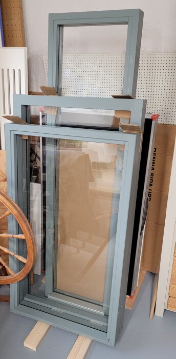Tre handgjorda fönsterkarmar staplade, blåmålade med glas och tätningslist.