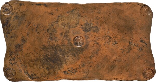 Ett gammalt, slitet kopparmynt, en koppardaler, placerad centrerat på en rostig yta.