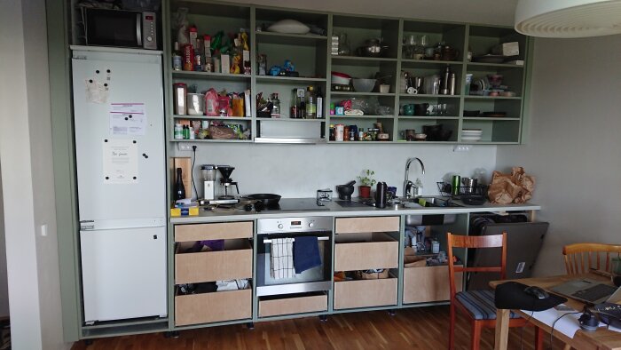 Kök under renovering med öppna lådor, avsaknad av luckor, synliga förvaringsartiklar och hushållsapparater.