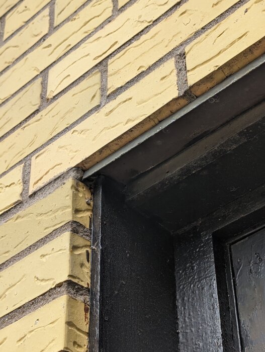 Bild på en gammal svart dörrkarm med sliten målning och gult tegel ovanför som behöver armering för större dörr.