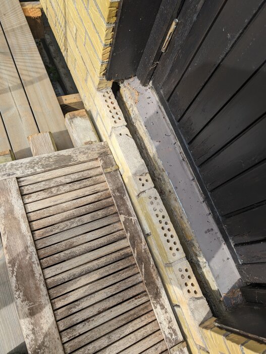 Delvis demonterad gammal dörrkarm och skadat tegelvägg ovanför en trätrappa, vid renoveringsarbete.
