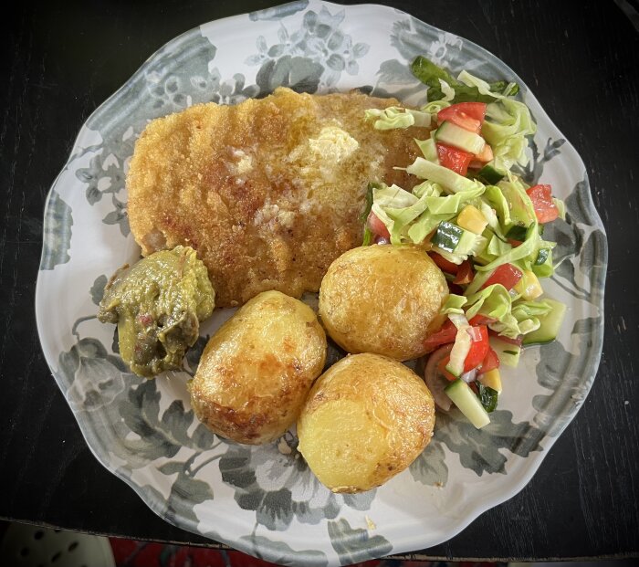 Schnitzel med ugnstekt potatis, guacamole och blandad sallad på ett mönstrat tallrik.