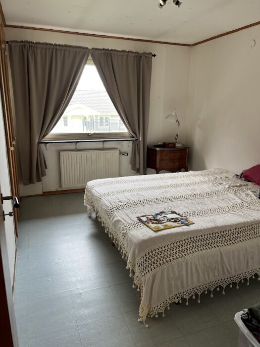 Sovrum i äldre stil med enkel säng, grått golv och vita väggar med synliga tecken på slitage.