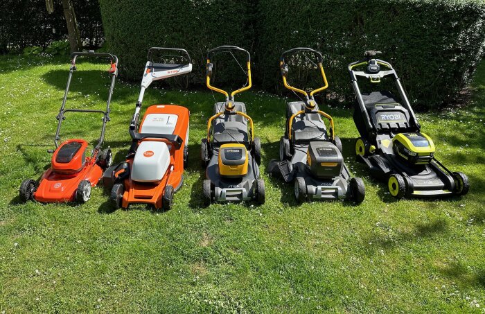 Fem olika modeller av batteridrivna gräsklippare uppställda på en gräsmatta.