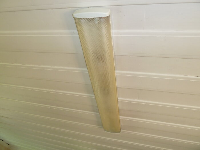 Gulnad skyddsplastkupa till lysrör monterad på vit panelvägg.