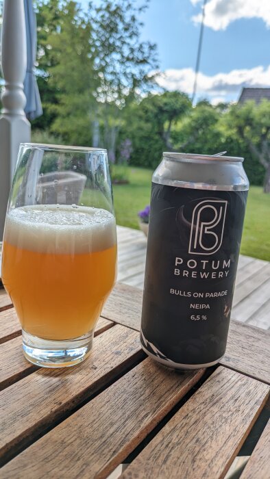 Ölglas och burk från Potum Brewery på träbord med trädgård i bakgrunden.