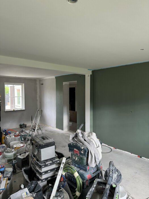 Renoveringsarbete i kök med synlig takbalk, gröna väggar och byggmaterial på golvet.