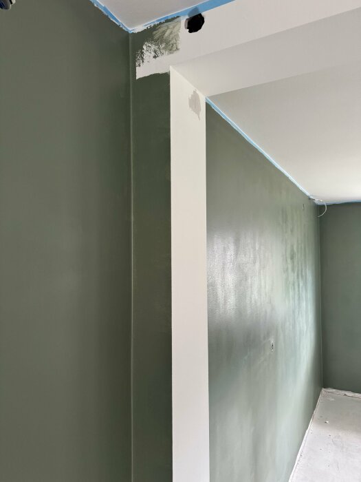 Hörn av ett ombyggt rum med en vit takbalk som möter grönmålade väggar.