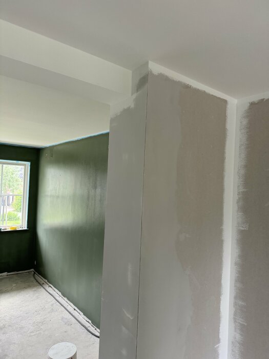Renoverat rum med grön vägg och en vitmålad balk i taket som möter en grå stödstruktur på väggen.