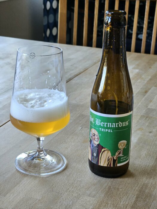 Öppnad flaska av St. Bernardus Tripel öl och ett halvtomt ölglas på bord.