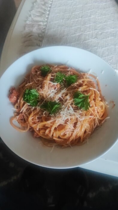 Tallrik med pasta och korv toppad med riven ost och färsk persilja.