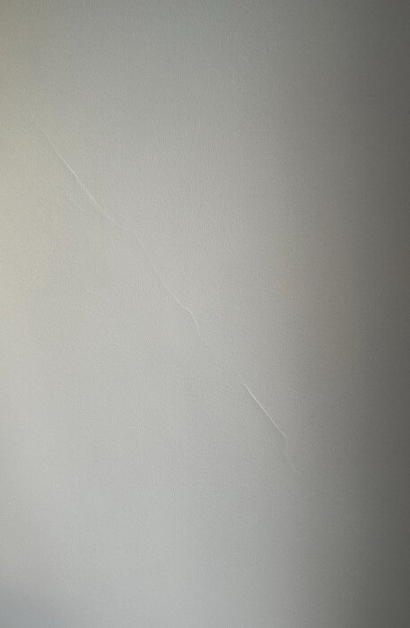Nybredspacklad vägg i vardagsrum med en synlig spricka som löper snett uppåt från ett nedre hörn.