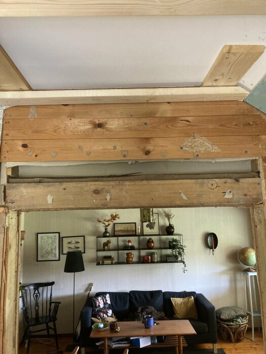 Husrenovering med synliga träbjälkar och råspont ovanför dörrpost i vardagsrum.