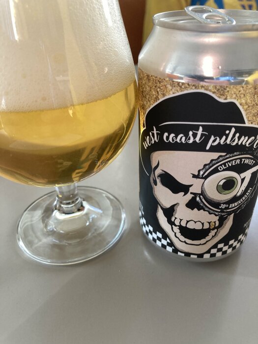 Ett glas öl bredvid en burk West Coast Pilsner, med en dödskalle på etiketten.