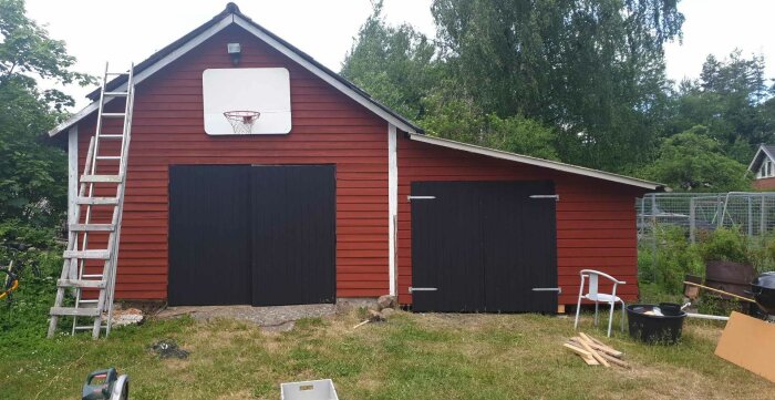 Renoverat rött garage med falurödfärgad vägg och två svartmålade dörrar, stege och byggmaterial i förgrunden.