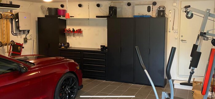 Garage interiör med Ikea plåtskåp, arbetsbänk, verktygstavla och rött fordon.