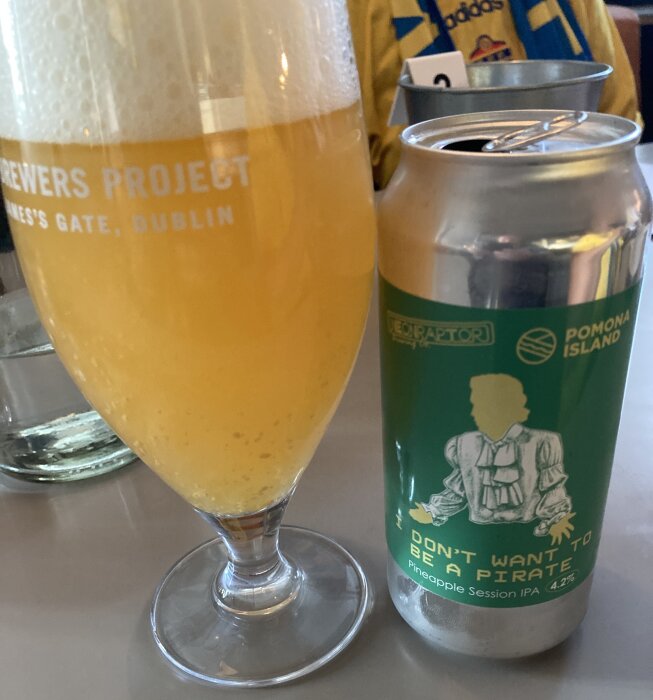 Ölglas fyllt med gul öl bredvid en burk Pomona Island Session IPA med ananassmak.