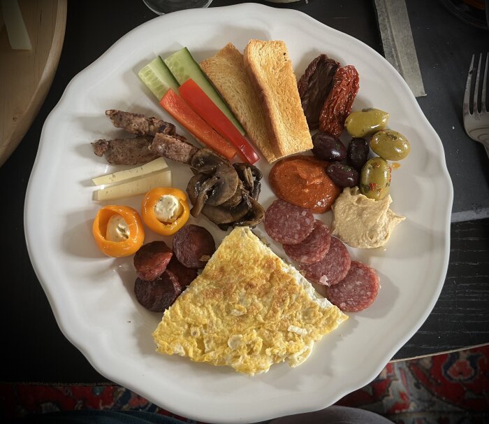 Frukosttallrik med potatiskaka, ostar, korv, hummus, soltorkade tomater, färsk frukt och grönsaker.