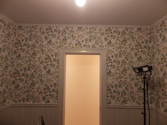 Renoverat rum med halvvägg av pärlspont och blommig tapet ovanför, detalj av dörrkarm och foder.