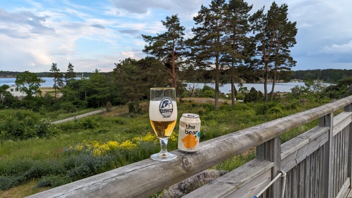 Ölglas med Falcon-öl och en burk öl på ett staket med utsikt över natur och vatten på Södra Finnö.