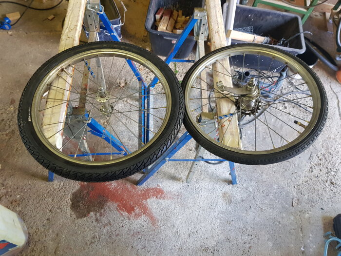 Två upprättade cykelhjul med nya däck och slangar på ett verkstadsgolv.