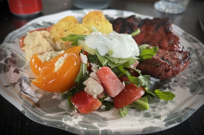 Grillad fläskkarré, ugnstekt potatis och färgglad sallad med hummus, tomat/chiliröra och tsatsiki på en tallrik.
