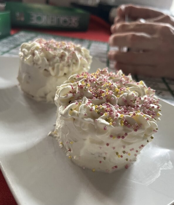 Två dessertbakelser med vispgrädde och strössel på ett vitt fat framför spelbrädet Sequence.