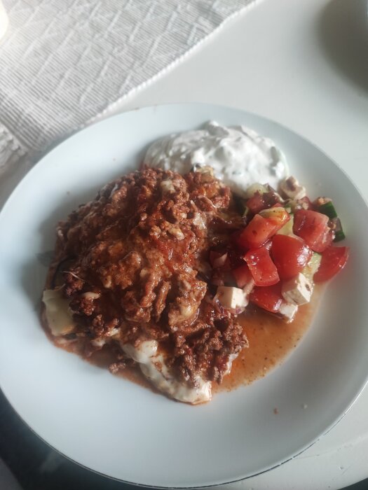 Portion moussaka med tzatziki och grönsallad på en tallrik.