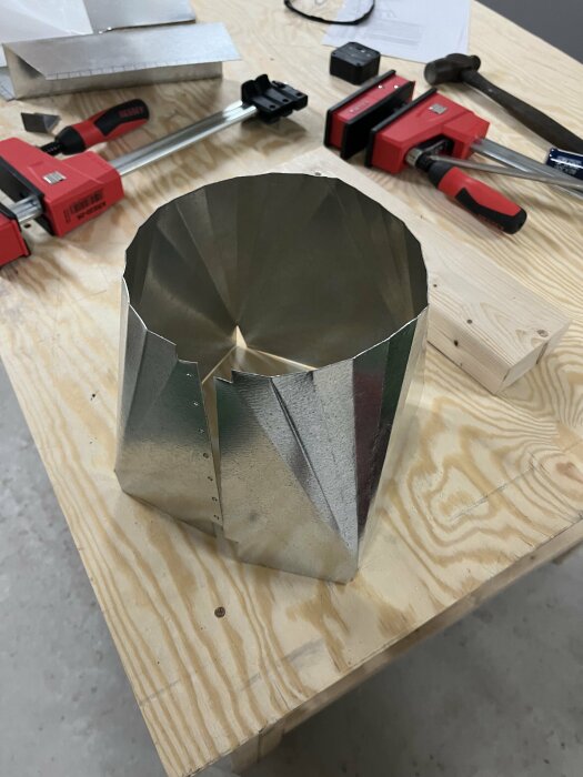 Metallövergång från kvadratisk till rund form på ett träbord med verktyg.