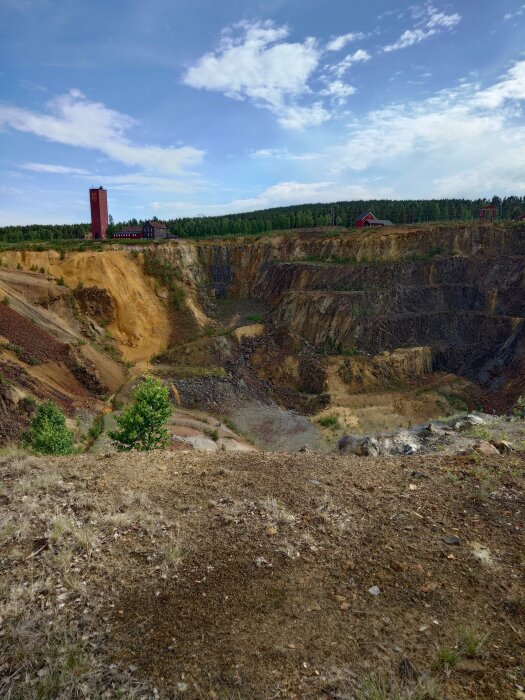 Utsikt över en stor gruvanläggning med röd tornbyggnad och skogsmark omkring.