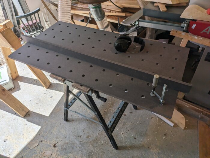 Valchromat MFT torsionsbox på ett arbetsställ med hål och en klämma, samt verktyg i en verkstad.