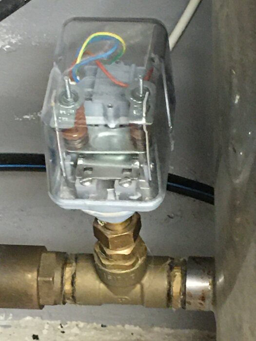 Rengjord tryckströmbrytare monterad på en vattenledning med synliga elektriska anslutningar och sladdar.